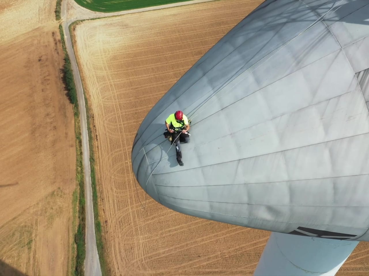 Vue plongeante sur un technicien encordé sur la nacelle, champs en contrebas